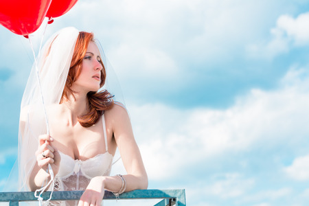 Bride with red balloons on balcony in lingerieの写真素材