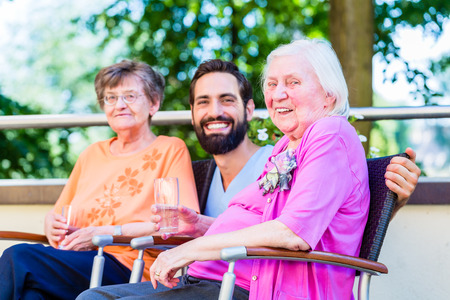 Nurse drinking coffee with seniors on terrace of retirement homeの写真素材