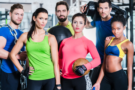 Group of women and men in gym posing at fitness training standing together with gear and dumbbells