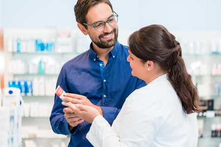 Pharmacist talking to customer in drug store, woman and man standing in front of shelvesの写真素材