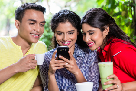 Indian girl showing pictures on smart phone to her friends in an Indian cafe