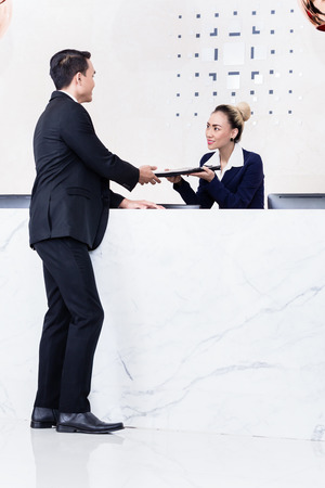 Job Applicant at business front desk giving his documents to receptionistの写真素材