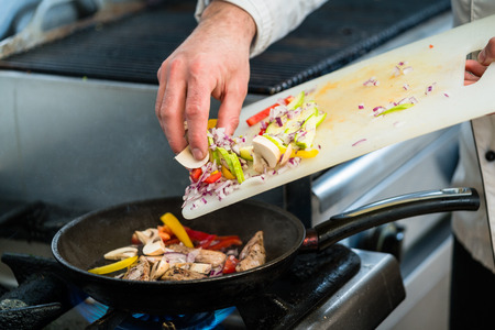 Chef putting ingredients to pan on cooker in restaurant kitchenの写真素材