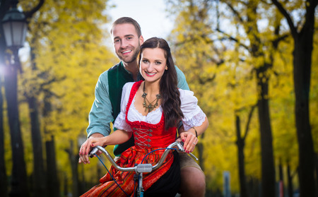 Man and woman in southern German Tracht riding bicycle together laughingの写真素材