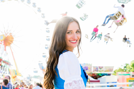 Dirndl wearing woman is standing in front of ferris wheel and carousel at Bavarian folk festivalの写真素材