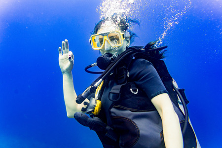 Woman scuba diving in her vacation on coral reef giving the ok signの写真素材