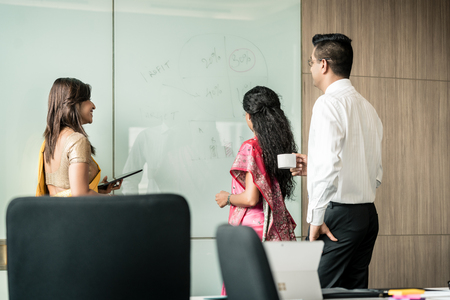 Three creative Indian colleagues writing ideas during brainstorming in the interior of a modern officeの写真素材