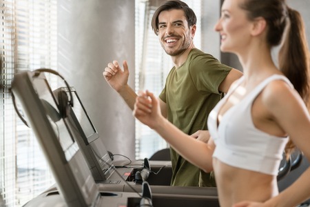 Determined young man smiling while running on treadmill during high-intensity interval trainingの写真素材