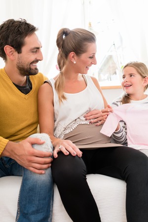 Mother, father and daughter awaiting family addition and looking at baby clothesの写真素材