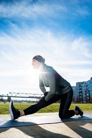 Low-angle view of a determined young woman stretching her leg while kneeling on a mat outdoors in...