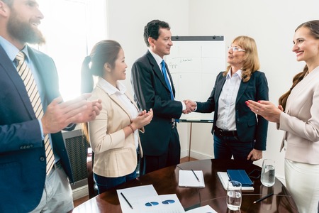 Two middle-aged business managers shaking hands as a gesture of congratulations for success and achievement during meeting in the conference roomの写真素材