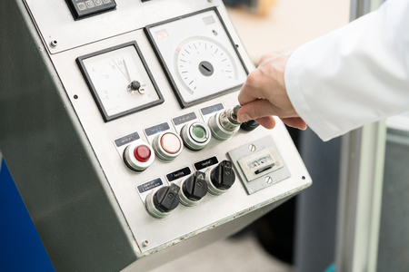 Close-up of the hand of a woman wearing white lab coat while turning on an industrial machine, with...