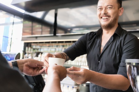 Friendly bartender serving espresso coffee to a middle-aged customer in the interior of a modern coffee shopの写真素材