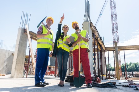 Low-angle view of a visionary architect pointing up while guiding and motivating two workers on the...