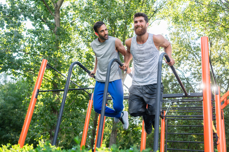 Low-angle view of two handsome young men passionate about fitness doing dips exercise for triceps in...