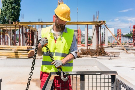 Reliable young worker checking the safety latch of a hook before lifting heavy weight with the crane...