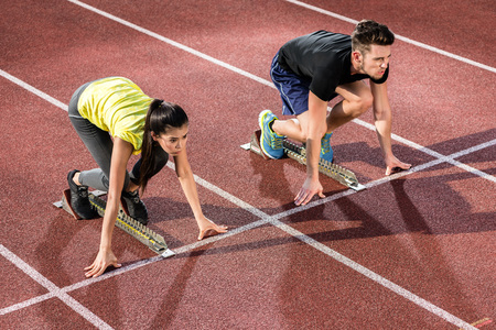 Male and female athlete in starting position at starting block of cinder trackの写真素材