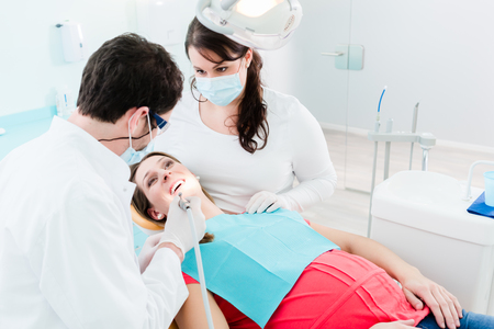 Dentist treating woman patient using drill on her teethの写真素材
