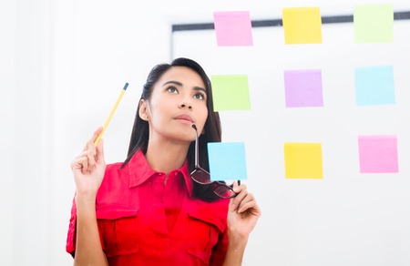 Portrait of young Asian employee looking at multiple reminders while planning her work in the office