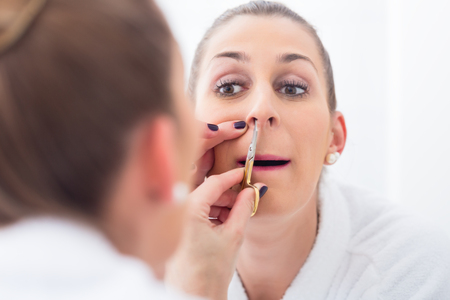 Young Woman in bathroom cutting her nostril hairの写真素材