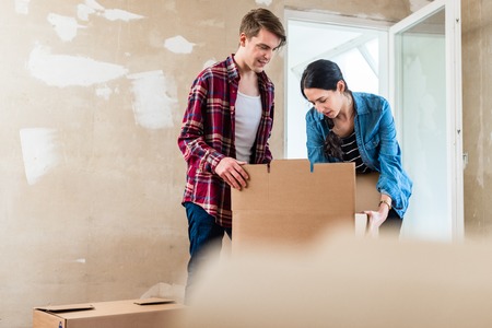 Young woman bringing an open heavy cardboard box while moving in with her boyfriend into their new homeの写真素材