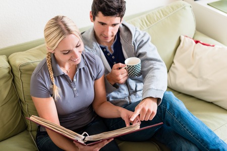 High-angle view of young nostalgic couple smiling while looking at a photo album together on sofa at homeの写真素材