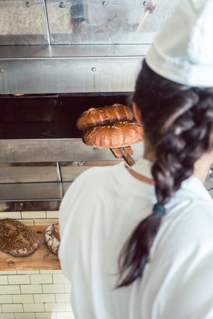 Baker woman getting fresh bread with shovel out of ovenの写真素材