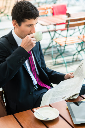 Young businessman smiling while reading a newspaper and drinking coffee in a cafeteria in the morningの写真素材
