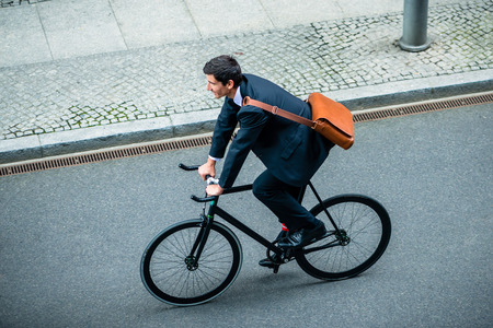 High angle view of young man wearing business suit while riding an utility bicycle on the streetの写真素材