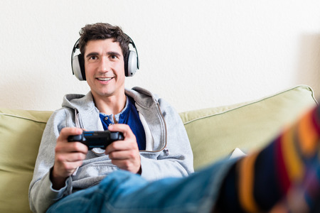 Happy young man using headphones while playing a video game on console in the living room at home