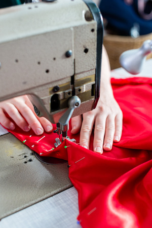Woman hands using sewing machine, addition of buttons, red fabric, fixing pinsの写真素材