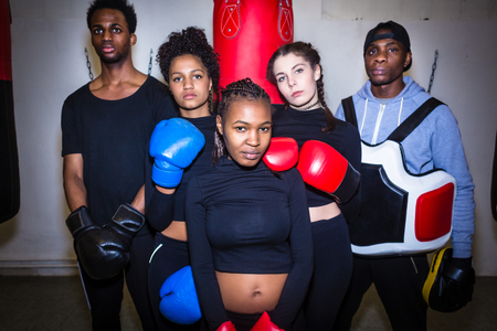 Portrait of four young determined boxers and their experienced boxing trainer looking at camera