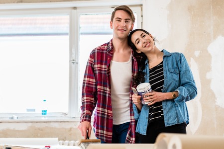 Portrait of a happy young couple wearing casual clothes while holding tools for home remodeling after moving in togetherの写真素材