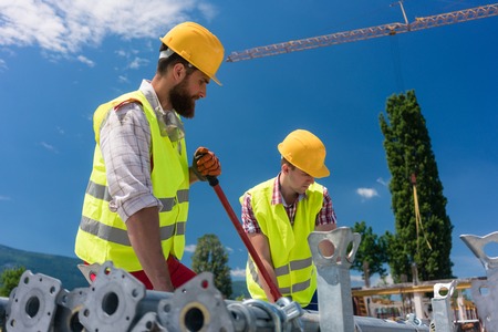 Two efficient blue-collar employees preparing supplies before building a metallic scaffolding while working together on the construction siteの写真素材