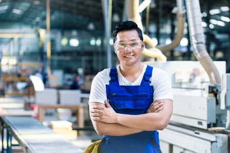 Worker in his carpenter workshop standing proud in front of the machines of the factory floorの写真素材
