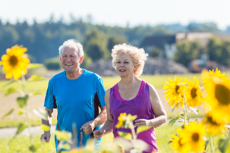 Cheerful senior couple with a healthy lifestyle jogging together side by side outdoors in the countryside in summerの写真素材