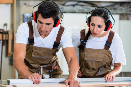 Carpenter and apprentice working together in wood workshopの写真素材