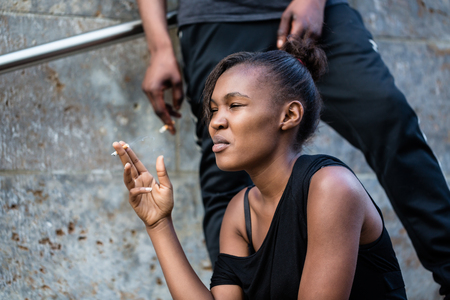 Young African American woman and man smoking outdoors in the cityの写真素材
