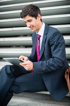 Young businessman smiling while using a tablet PC for online communication or data storage outdoorsの写真素材