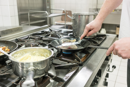 Cook or chef in Restaurant frying carp fish in pan on stoveの写真素材