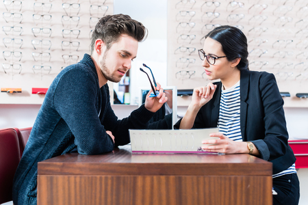 Man at optician shop getting advice from sales womanの写真素材