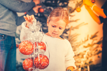 Young girl helping decorating the Christmas tree, holding some Christmas baubles in her handの写真素材
