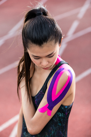 Woman taping with therapeutic tape on cinder track of sports stadiumの写真素材