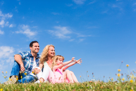 Dad, Mom and daughter sitting in meadow, asymmetric left, total viewの写真素材