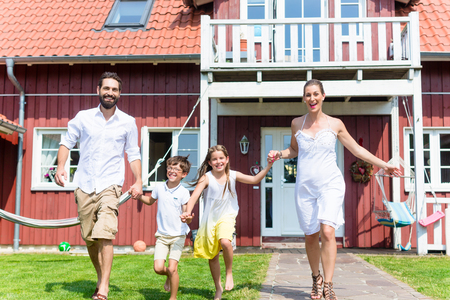 Happy family running on meadow in front of house on front yard grassの写真素材