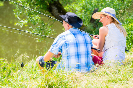 Couple, woman and man, sitting at river side with fishing rods angling for sportの写真素材