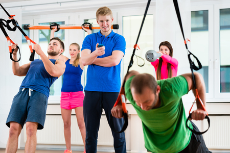 Group of men and women in gym doing workout at rings supervised by physioの写真素材