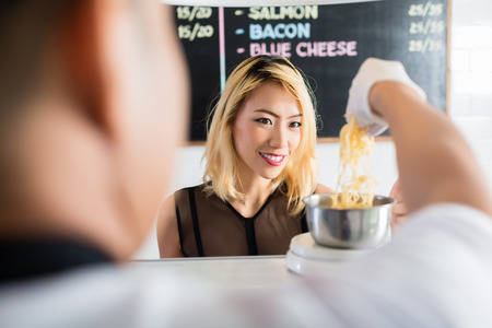 Asian woman watching intently as grated cheese is placed on a scale for weighing in a restaurant or deli in an over the shoulder view from behind the shop assistantの写真素材