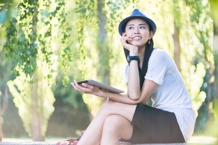 Young Asian woman smiling while using a tablet PC outdoors in the parkの写真素材