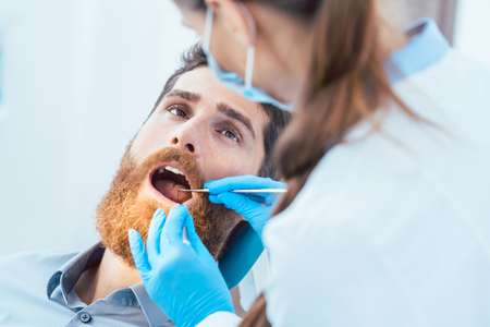 Side view of a reliable female dentist, using sterile instruments and blue surgical gloves while cleaning the teeth of a patient in the dental office of a modern clinicの写真素材